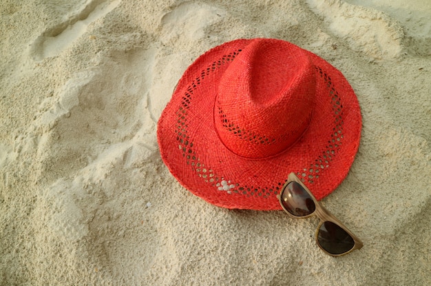 Sombrero de paja rojo con gafas de sol marrones en la playa de arena