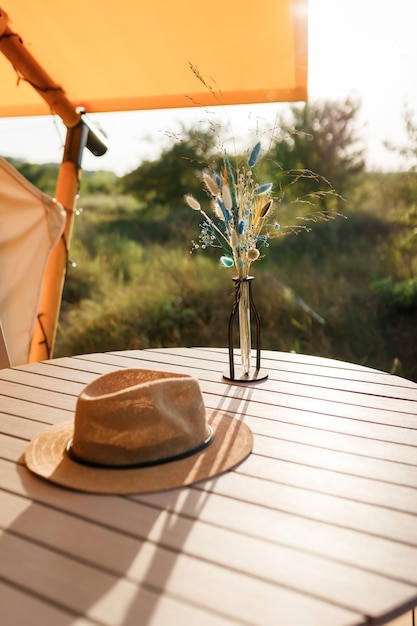 Sombrero de paja tirado en la mesa afuera cerca de la carpa glamping durante el día de verano