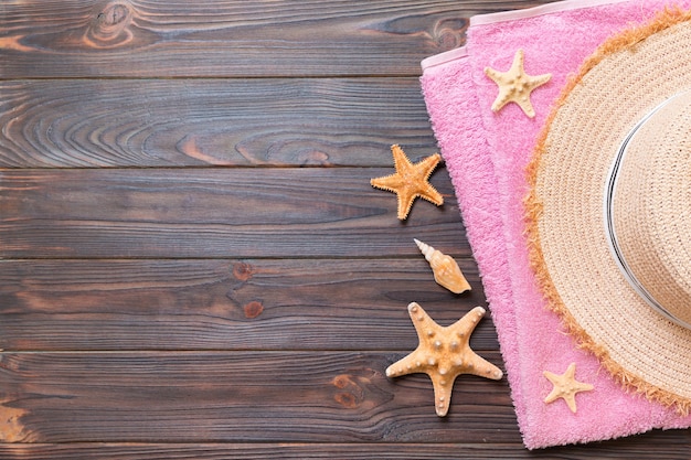 Sombrero de paja, toalla rosa y estrella de mar sobre un fondo de madera oscura. concepto de vacaciones de verano de vista superior con espacio de copia.