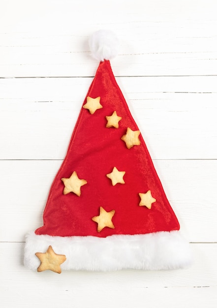 Foto sombrero de papá noel decorado con galletas en forma de estrella como creativo árbol de navidad sobre fondo de madera blanca.