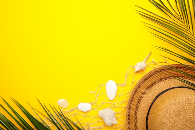 Foto sombrero de playa con conchas marinas y hojas de palma sobre fondo amarillo