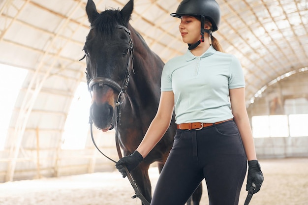 Foto en sombrero protector una mujer joven con ropa de jockey se prepara para un paseo con un caballo en un establo