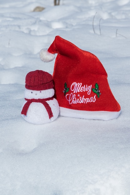 Sombrero rojo de Navidad y un encantador juguete de muñecos de nieve en el concepto de celebración navideña de nieve blanca