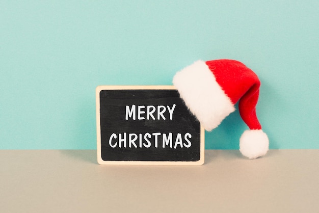 Sombrero rojo de Papá Noel colgado en una pizarra, tarjeta de felicitación con deseos de feliz navidad, invierno