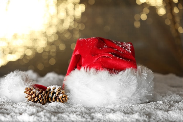 Sombrero rojo de Santa Claus con piñas en la nieve artificial contra el fondo dorado, cerrar