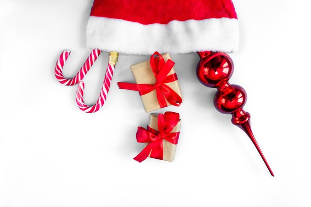 Sombrero de Santa Claus con bastones de caramelo, juguetes y cajas de regalo sobre un fondo blanco.