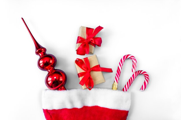 Sombrero de Santa Claus con bastones de caramelo, juguetes y cajas de regalo sobre un fondo blanco.