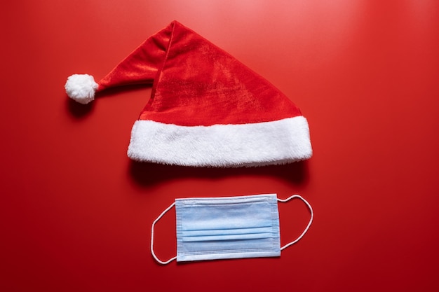 Sombrero de santa claus y máscara médica sobre un fondo rojo.