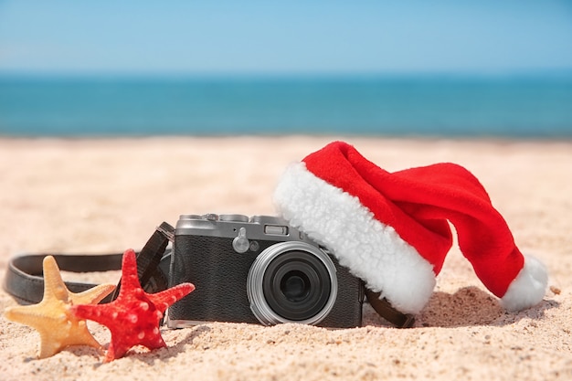 Sombrero de Santa con estrellas de mar y cámara en la playa. Concepto de vacaciones de Navidad