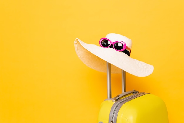 Sombrero para el sol y gafas de sol en el asa de la maleta sobre fondo amarillo