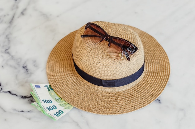 Sombrero para el sol con gafas de sol y billetes de cien centésimas de euro. Concepto de vacaciones