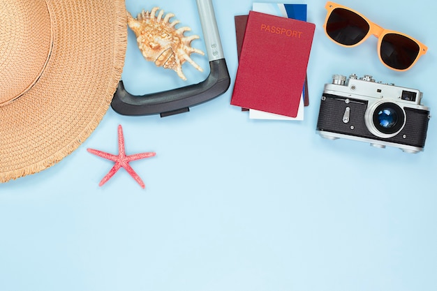 Sombrero para el sol, maleta, concha, estrella de mar, entradas, pasaporte, gafas y cámara sobre fondo azul claro. concepto de viaje