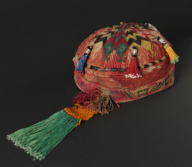 Sombrero de solideo asiático tradicional colorido con coletas sobre un fondo oscuro