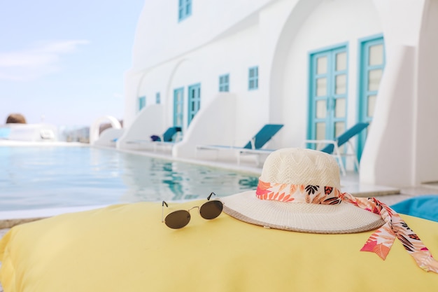 Sombrero de verano y gafas de sol en un puf amarillo con fondo de piscina