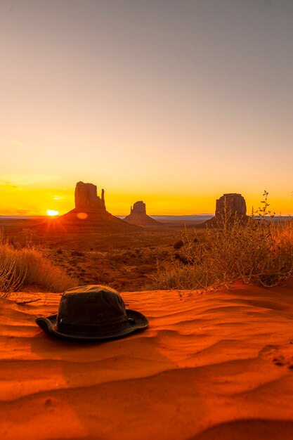 Foto un sombrero verde sobre la arena roja al amanecer en monument valley, utah. foto vertical