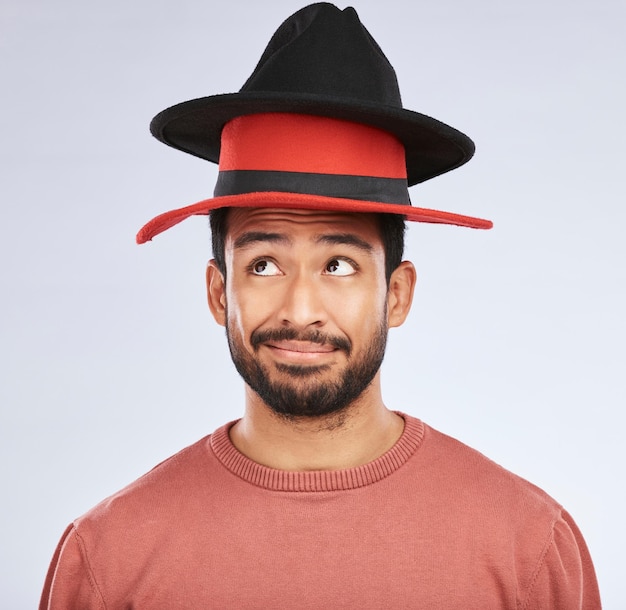 Sombreros confundidos y hombre joven en un estudio con una idea de pensamiento o contemplando la expresión de la cara Persona masculina pensativa e india con divertidos accesorios para la cabeza aislados por un fondo blanco