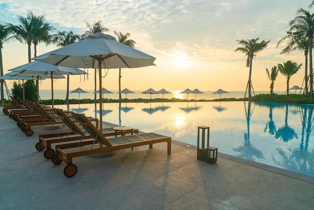 Sombrilla con piscina de cama alrededor de la piscina con fondo de mar océano al atardecer o al amanecer - concepto de vacaciones y vacaciones