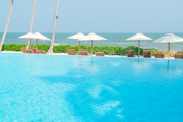 Sombrilla con piscina de cama alrededor de la piscina con fondo de mar océano - concepto de vacaciones y vacaciones