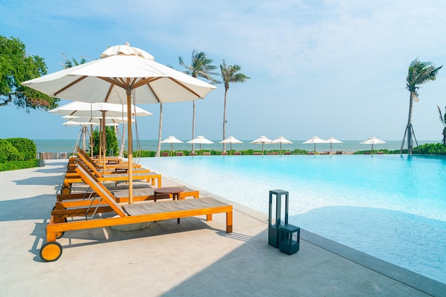 Sombrilla con piscina de cama alrededor de la piscina con fondo de mar océano - concepto de vacaciones y vacaciones