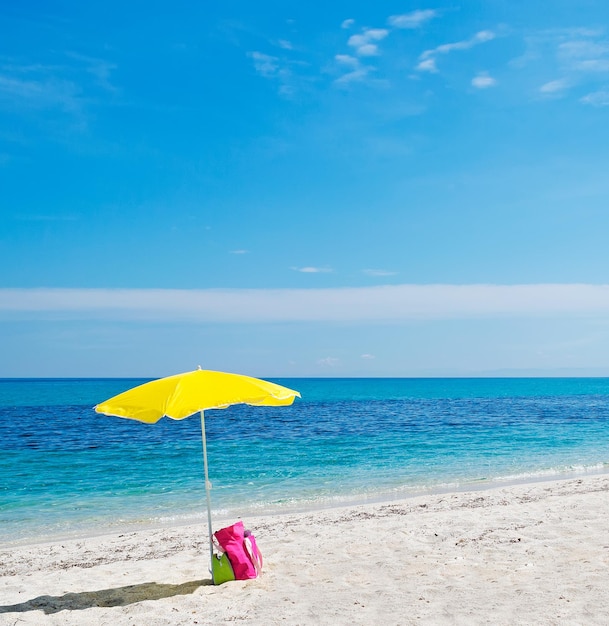 Sombrilla de playa amarilla y bolso rosa bajo un cielo azul