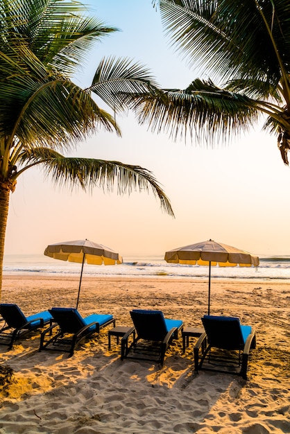 Sombrilla de playa con palmeras y playa al amanecer - concepto de vacaciones y vacaciones