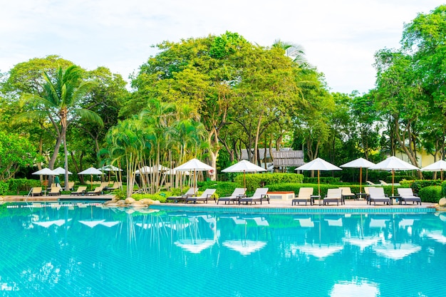 Sombrilla y silla alrededor de la piscina en el hotel resort para viajes de placer y vacaciones cerca de la playa del océano al atardecer o al amanecer.