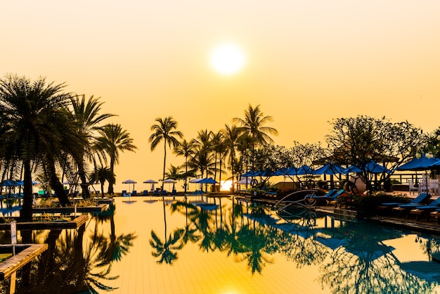 sombrilla y silla en la piscina con palmeras al amanecer