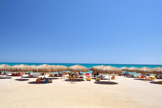 Sombrillas de paja en la playa tropical del mar con tumbonas de descanso contra el cielo azul vibrante en verano