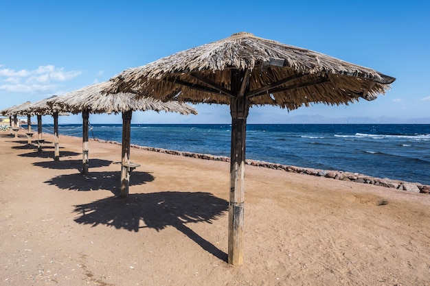 Sombrillas de playa de madera y tumbonas junto al mar rojo en un día soleado