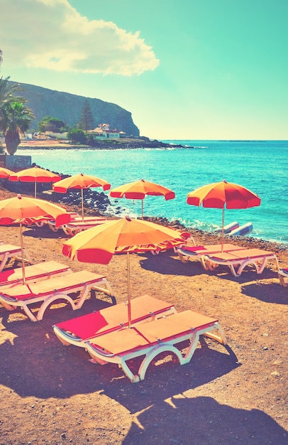Sombrillas y tumbonas vacantes en una playa de mar, Tenerife. Imagen filtrada de estilo retro