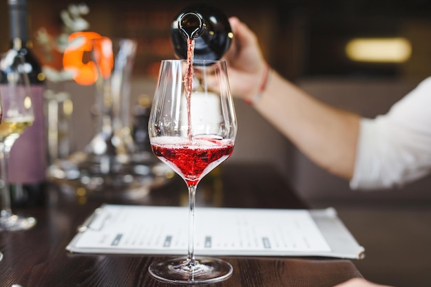 Sommelier habilidoso com relógio de pulso derrama vinho tinto em copo de vinho elegante durante degustação sentado à mesa no restaurante de luxo vista de perto