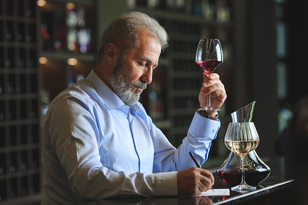 Un sommelier senior está probando vino tinto.