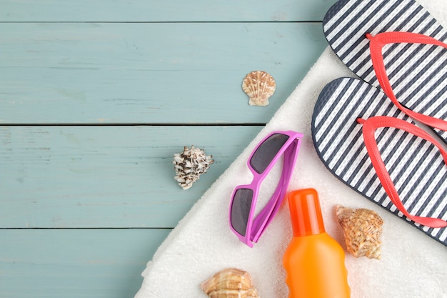 Sommer Accessoires. Strandzubehör. Ohrfeigen, Handtuch und Sonnenbrille auf einem blauen Holztisch. Ansicht von oben.