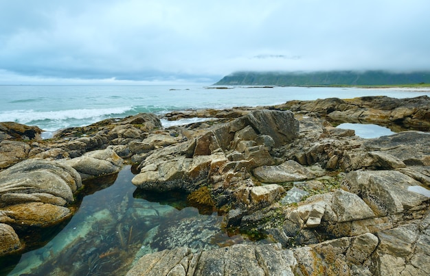 Sommer bewölkter Blick auf den Strand mit Pool inmitten von Steinen (Ramberg, Norwegen, Lofoten).