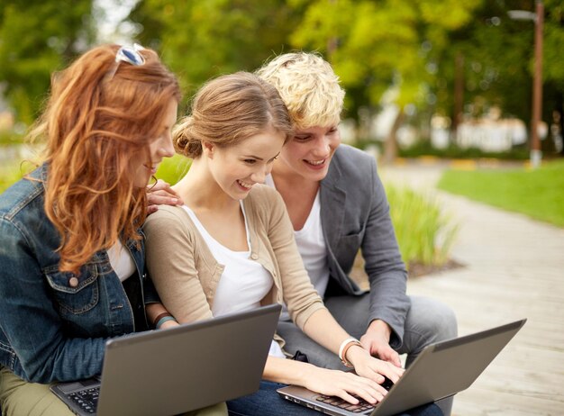 sommer-, bildungs-, technologie- und menschenkonzept - gruppe von studenten oder jugendlichen mit laptops, die draußen auf einer bank sitzen