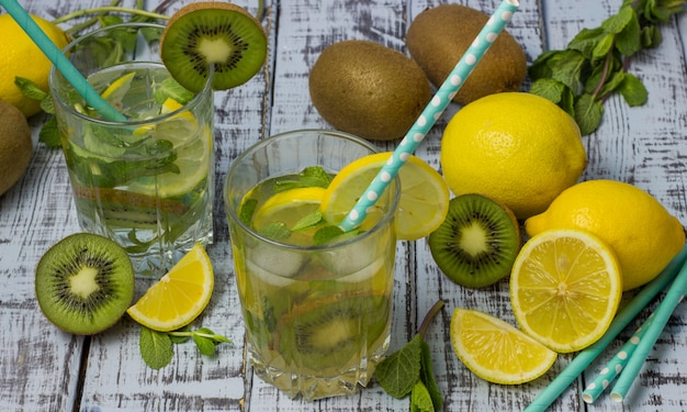 Sommer-Erfrischungsgetränk in Gläsern mit einem Strohhalm. Kalte süß-saure Limonade mit Zitrone, Kiwi, Minze und Eiswürfeln auf einem grauen Holztisch.