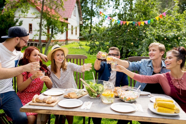 Sommer, Feiertage, Feierleute und Essenskonzept - glückliche Freunde, die eine Gartenparty feiern und Gläser anstoßen