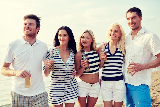 sommer, ferien, tourismus, getränke und personenkonzept - gruppe lächelnder freunde mit flaschen, die bier oder apfelwein am strand trinken