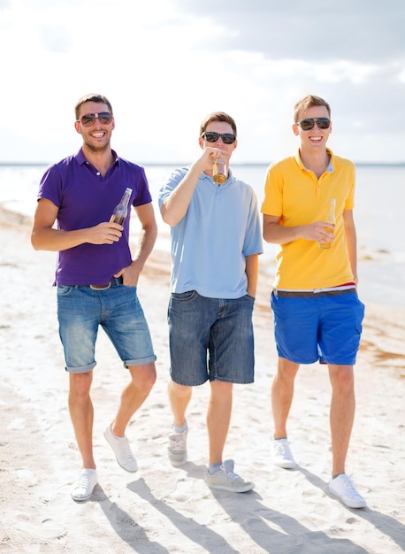 sommer, ferien, urlaub und menschenkonzept - gruppe männlicher freunde, die sich am strand mit flaschen bier oder alkoholfreien getränken amüsieren