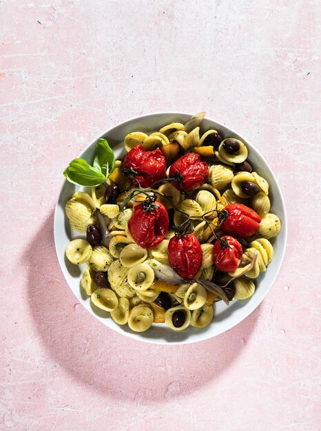 Sommer italienische Pasta Orecchiette mit gebackenen Tomaten Oliven und Pesto auf rosa Hintergrund