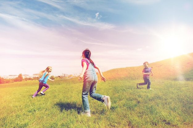 Sommer, Kindheit, Freizeit und Menschenkonzept - Gruppe glücklicher Kinder spielen Tag-Spiel und laufen auf grünem Feld im Freien