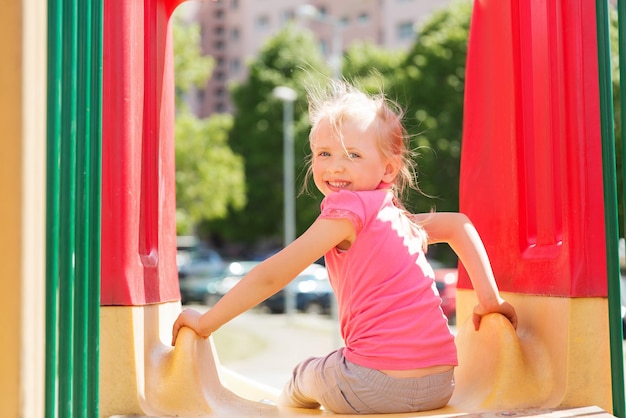 Sommer-, Kindheits-, Freizeit- und Menschenkonzept - glückliches kleines Mädchen auf Rutsche auf dem Kinderspielplatz