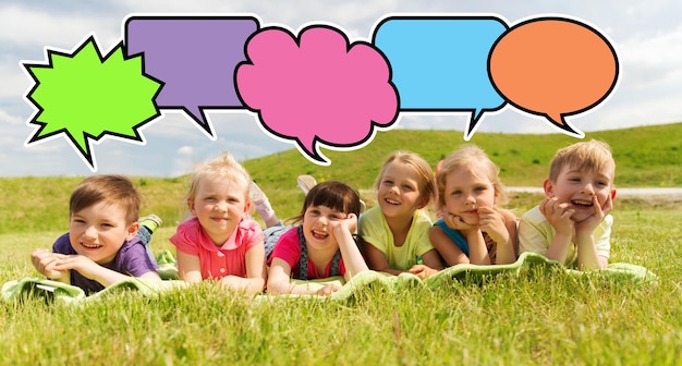 Foto sommer-, kindheits-, freizeit- und personenkonzept - eine gruppe glücklicher kinder, die auf einer decke liegen oder im freien mit bunten textblasensymbolen bedeckt sind