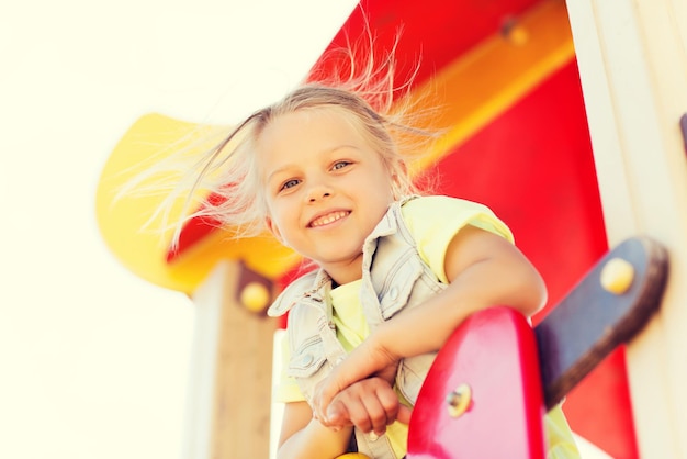 sommer-, kindheits-, freizeit- und personenkonzept - glückliches kleines mädchen auf kinderspielplatz-klettergerüst