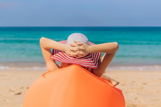 Sommer-Lifestyle-Porträt eines hübschen Mädchens, das auf dem orangefarbenen aufblasbaren Sofa am Strand der tropischen Insel sitzt Entspannen und das Leben auf dem Luftbett genießen