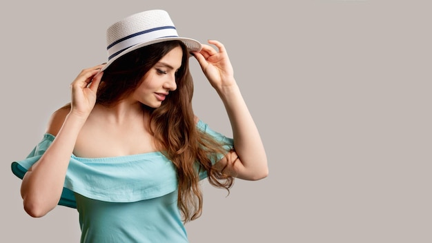 Sommer-Look Weibliche Eleganz Hübsche lächelnde Frau in schulterfreiem blauem Kleid und weißem Hut isoliert auf neutralem Kopierraum Urlaubsoutfit Sonnenschutz