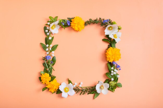 Sommer- oder Frühlingskomposition auf Orangr-Hintergrund Quadratischer Rahmen aus Blumen und Blättern mit Draufsicht auf den Kopierbereich Blumenkonzept des Sommerfrühlings