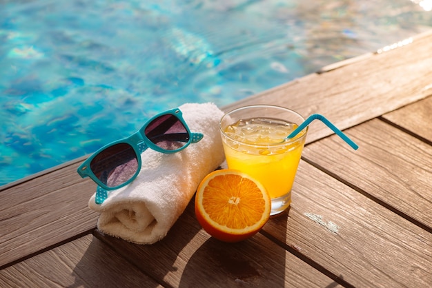 Sommer-Orangensaft-Hut und Sonnenbrille entspannen sich in der Nähe des Swimmingpools.