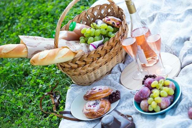 Sommer - Picknick auf der Wiese im Park. Baguette, Wein, Gläser, Trauben und Brötchen in einem Korb auf grünem Gras