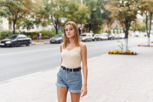 Sommer sonniges Lebensstilmodeporträt der jungen stilvollen Hipsterfrau, die auf der Straße geht, lächelnd